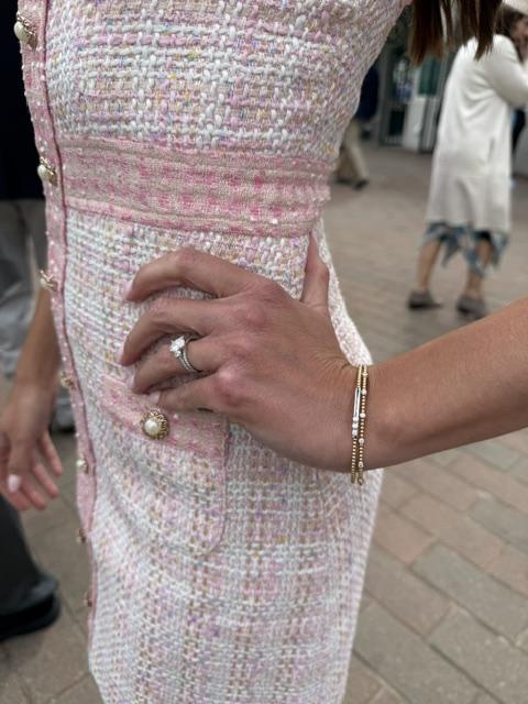 Engagement ring and gold bracelet stack photographed against pink tweed dress detail