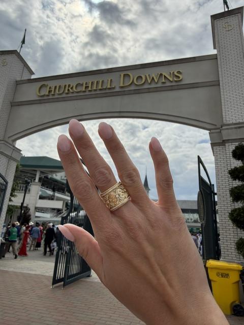 Hand wearing the 18K yellow gold diamond fashion ring framed by the Churchill Downs sign